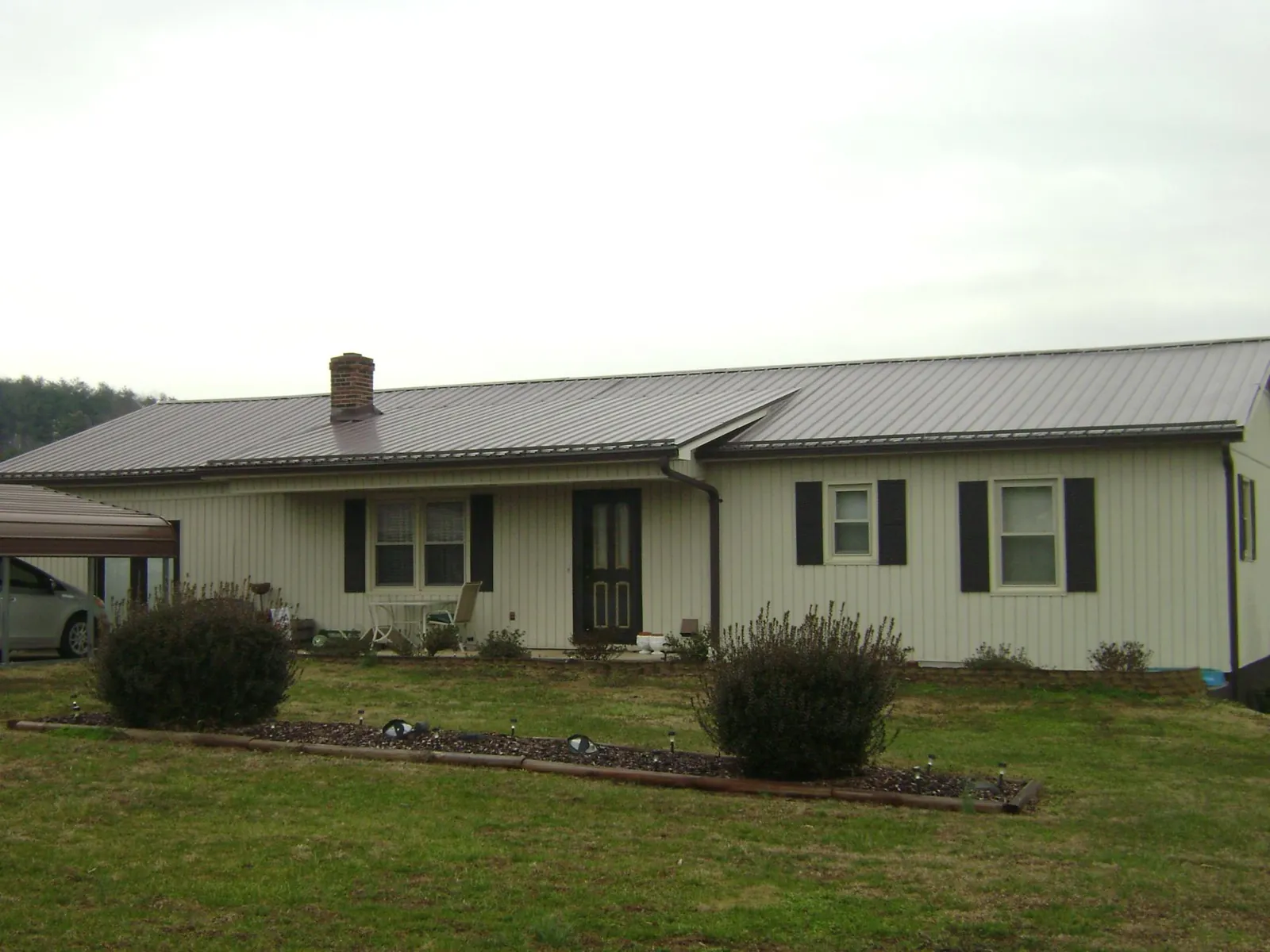 Brown metal roof on a cream sided ranch home with a brick chimney in Marlborough
