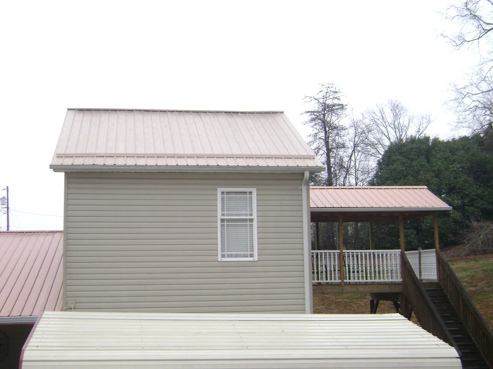 Tan metal roofs on a two story addition and attached porch, from a Roof Replacement job in Marlborough